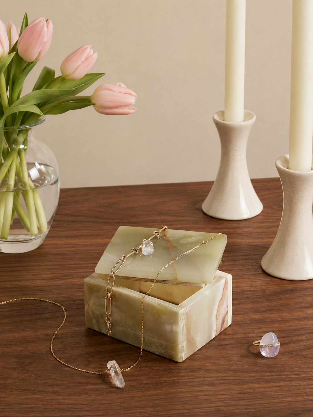 Green onyx jewelry box with necklace and ring on a wooden table with pink tulips and candles in the background.